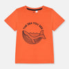 Child wearing an orange t-shirt with a whale graphic and text on a beige background
