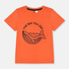 Child wearing an orange t-shirt with a whale graphic and text on a beige background