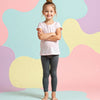 Young girl wearing a white t-shirt and dark leggings standing against a colorful abstract background.