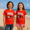 Two children wearing red 'Shark Attack' t-shirts on a beach.