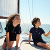 Two children on a sailboat with clear blue sky and ocean.