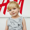 Child wearing a gray sleeveless shirt with dinosaur prints in front of a red and white logo.