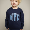 Child wearing a navy blue sweatshirt with 'NYC' in light blue letters on a beige background