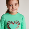 Young girl wearing a green long-sleeve shirt with butterfly design on a plain background