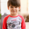 Child wearing a red and gray shirt with a car design, standing indoors.