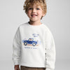 Child wearing a white sweatshirt with a blue truck graphic and text on a gray background