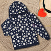 Child wearing a navy blue hoodie with white floral patterns sitting on yellow grass.