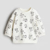 Child wearing a cream sweater with black patterns and dark pants on a light gray background