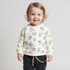 Child wearing a cream sweater with black patterns and dark pants on a light gray background