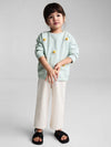 Child wearing a light blue sweater with daisy flowers, sitting on a small wooden stool against a plain background.