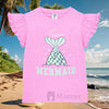 Young girl wearing a pink 'Mermaid' t-shirt on a beach with palm trees and ocean in the background.